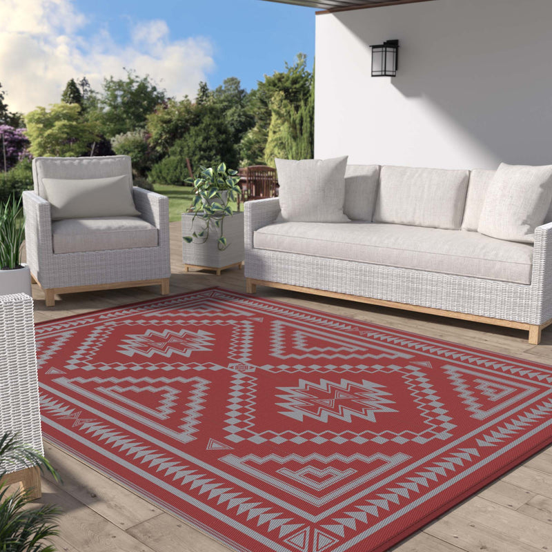 Calvex Diamond Geometric Reversible Outdoor Rug Red Gray placed on a paving stone courtyard floor