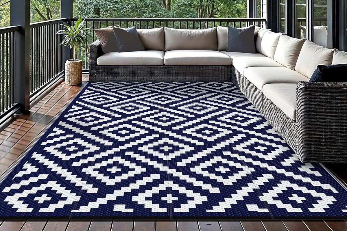 Navy and white Cadris Double-Sided Rhombic Outdoor Rug under a wicker sectional sofa on a covered wood deck