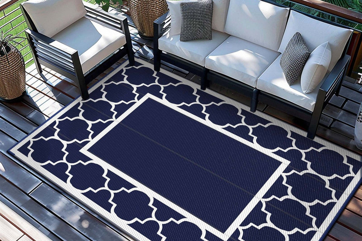 Axora Symmetrical Geometric Reversible Outdoor Rug in navy and white under a white outdoor sofa set on a dark deck